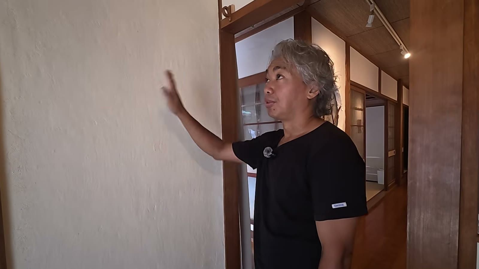 瀬居島の宿で、漆喰の壁に手を当てて話す宮前
